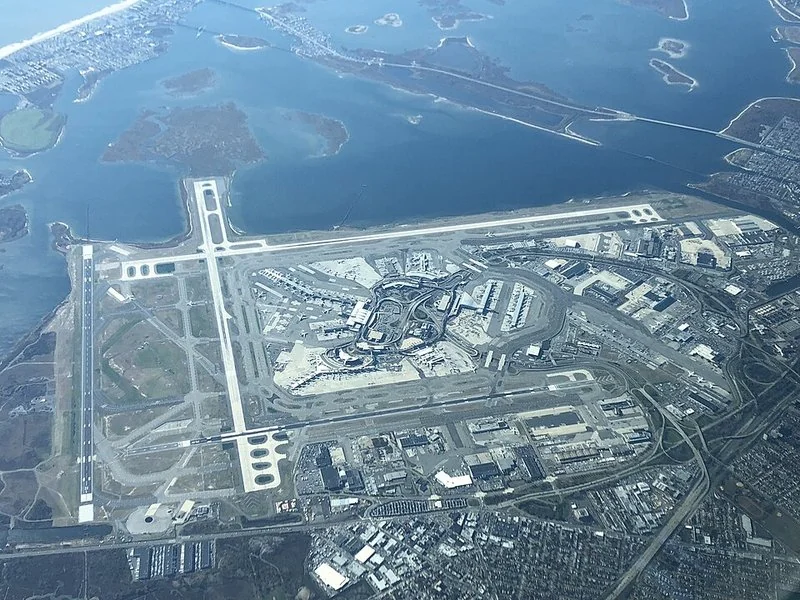 como ahorrar en jfk, Vista aérea del aeropuerto internacional John F. Kennedy de Nueva York, con sus terminales, pistas y accesos viales sobre la bahía.