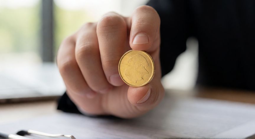 Mano sosteniendo una moneda de oro brillante sobre un escritorio financiero