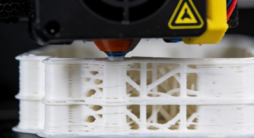 como ahorrar filamento, Boquilla de impresora 3D extruyendo filamento blanco mostrando capas y relleno interno