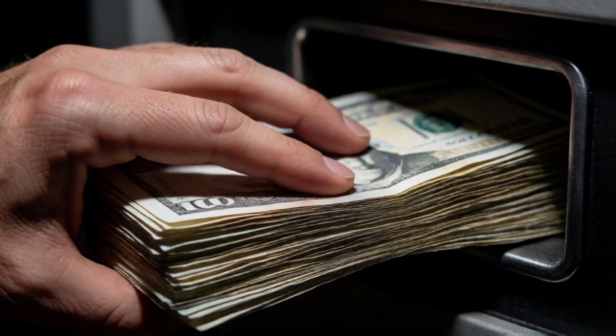 como ahorrar un millon en un año, Mano guardando un gran fajo de billetes en una caja fuerte metálica