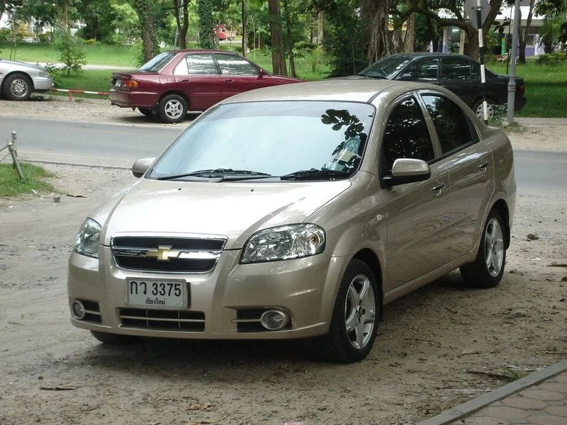 Chevrolet Aveo sedán dorado estacionado en la calle, visto de frente y lateral