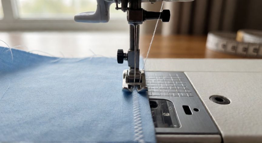 como coser a máquina para que no se deshilache la tela, Aguja de máquina de coser realizando puntada zigzag en el borde de una tela de algodón azul