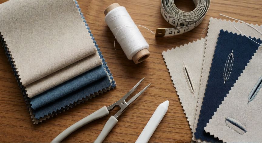 como coser ojales a maquina, Materiales de costura sobre mesa de madera: retales de tela, hilo, deshilachadora y muestras de ojales cosidos