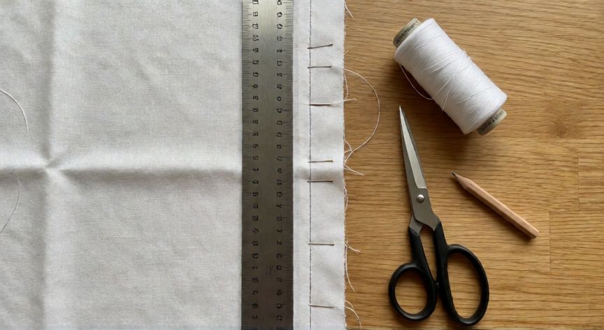 como coser recto a mano, Mesa de costura con tela cosida recta a mano, regla metálica, alfileres y bobina de hilo blanco