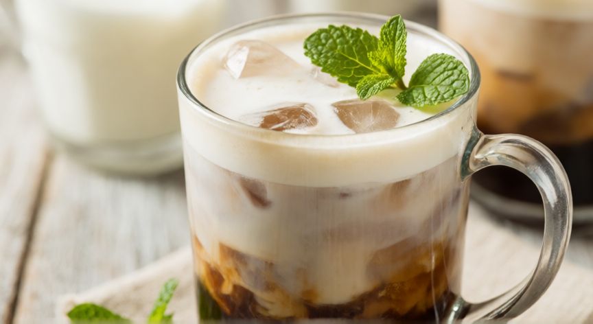 como hacer cafe bomba keto, Vaso de café bomba keto con espuma cremosa y hielo sobre mesa de madera