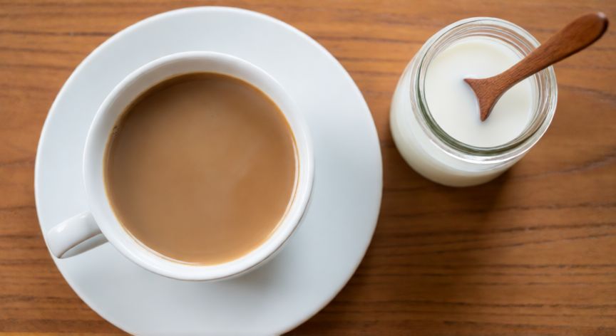 como hacer cafe flat white, Vista cenital de un flat white terminado en taza blanca sobre mesa de madera