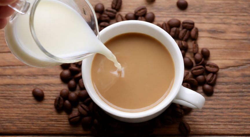 como hacer café instantáneo con leche, Taza de café con leche viéndose la cremosidad sobre mesa de madera