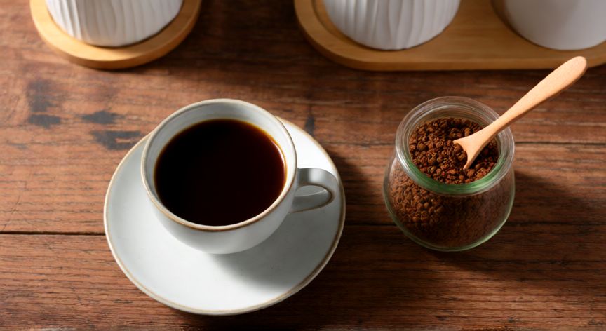 como hacer cafe instantaneo nescafe, Taza de café Nescafé servido con frasco de granos en mesa de madera
