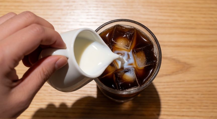 como hacer café latte frío en casa, Vertiendo leche fría sobre café con hielo para preparar latte