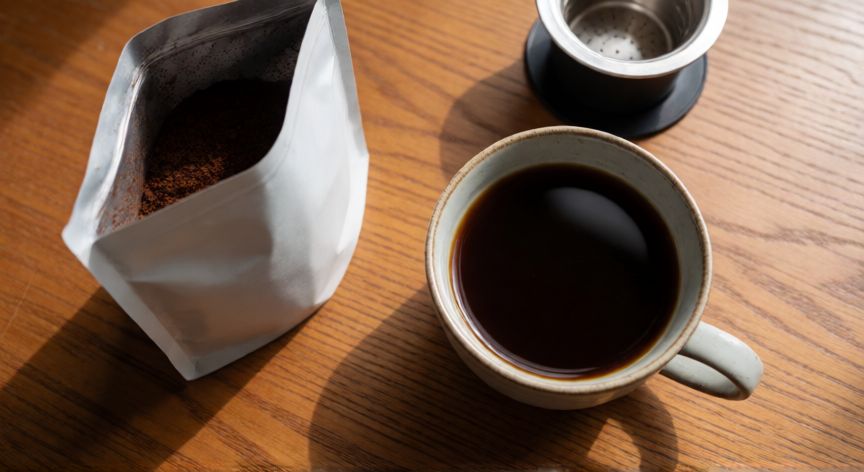como hacer cafe molido en cafetera philips, Taza de café recién hecho junto a café molido y filtro reutilizable