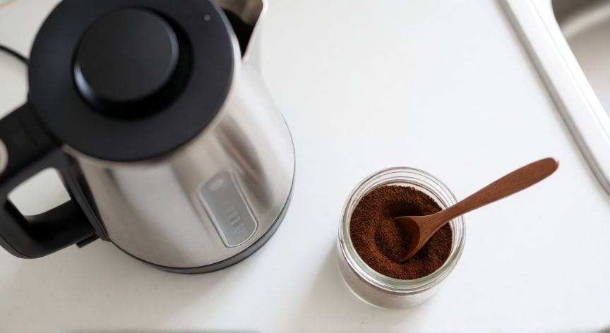 como hacer cafe rapido, Hervidor eléctrico moderno junto a un bote de café molido en una cocina limpia