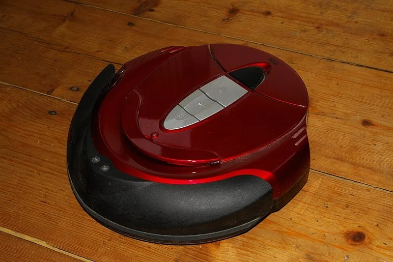 Robot aspirador rojo con torreta láser sobre suelo de madera