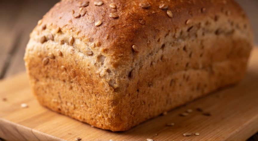 como hacer pan sarraceno en casa, Pan de sarraceno recién horneado con corteza dorada y semillas sobre tabla de madera