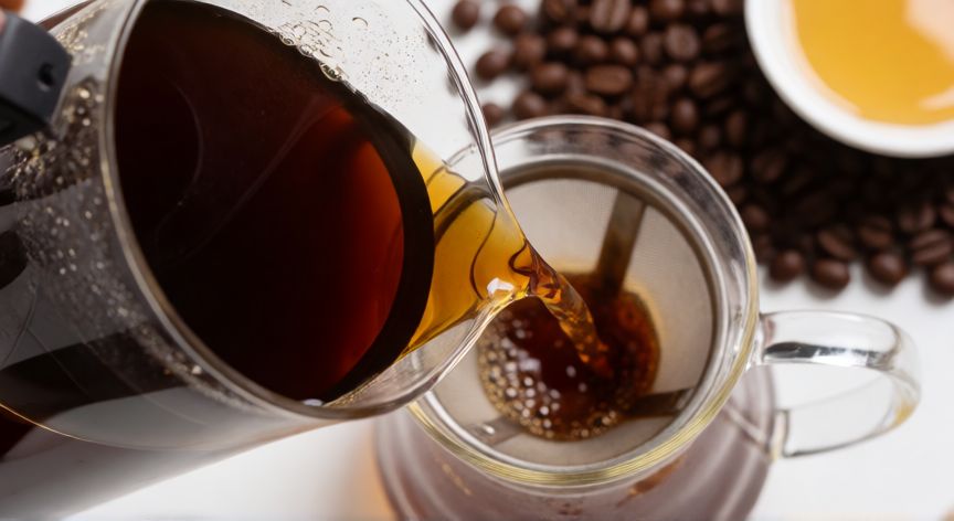 como hacer un cafe para quitar el sueño, Proceso de filtrado de café oscuro con canela y miel al fondo