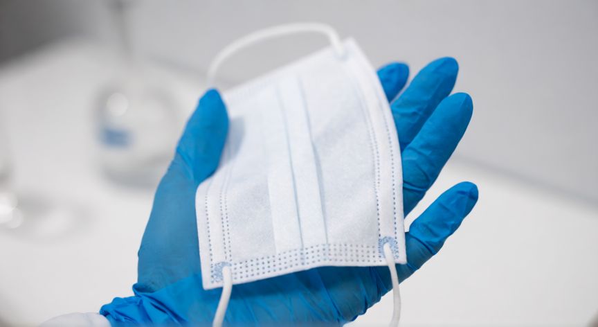 covid 19 5 years ago, Manos con guantes médicos sosteniendo una mascarilla de protección en un entorno clínico
