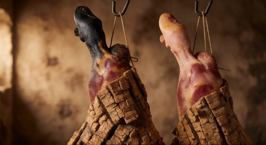 diferencia entre jamon iberico y serrano, Pies de jamón ibérico y serrano colgados en sala de curación