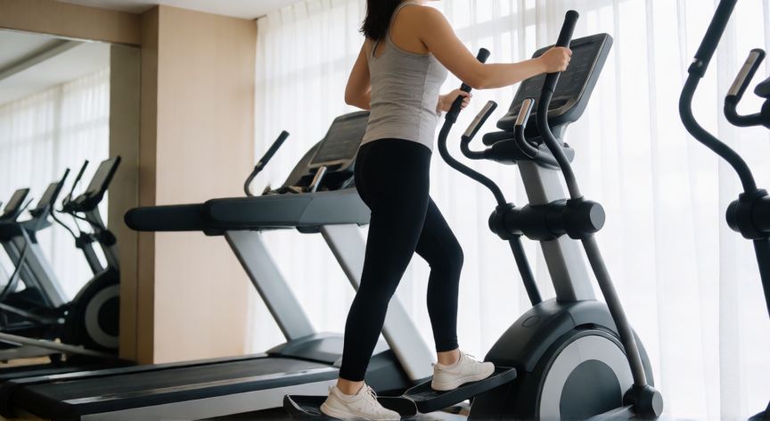 es mejor correr o eliptica, Mujer ejercitándose en máquina elíptica en gimnasio moderno