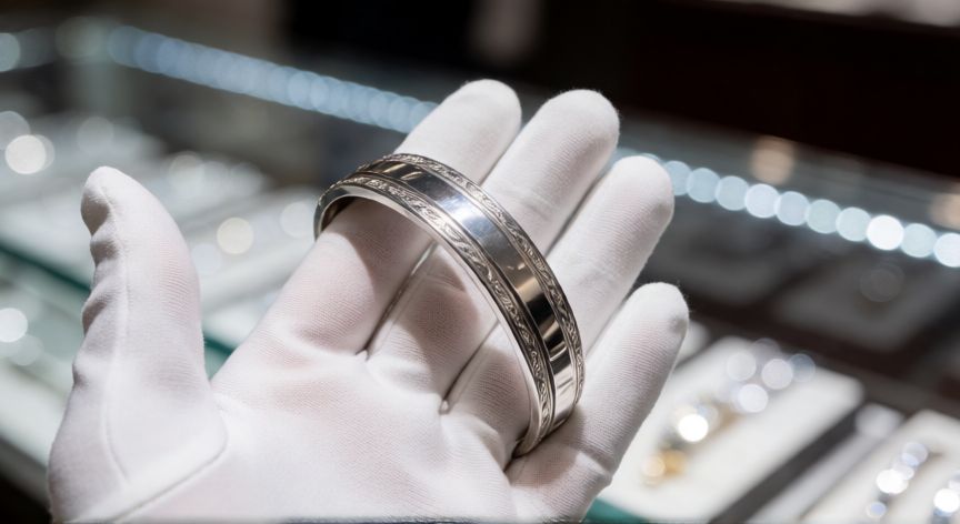 mejor producto para limpiar la plata, Mano con guante blanco sosteniendo una pulsera de plata brillante y pulida tras la limpieza