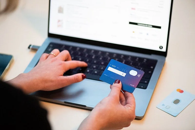 mejor producto para vender en shopify, Persona comprando online con tarjeta bancaria frente a un portátil con una tienda abierta