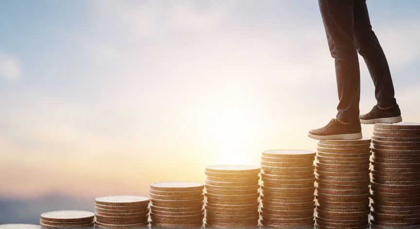 por qué ahorrar es importante, Persona subiendo una escalera de monedas hacia un horizonte brillante simbolizando libertad financiera