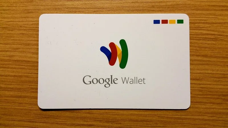 Tarjeta física de Google Wallet con logotipo multicolor sobre fondo de madera