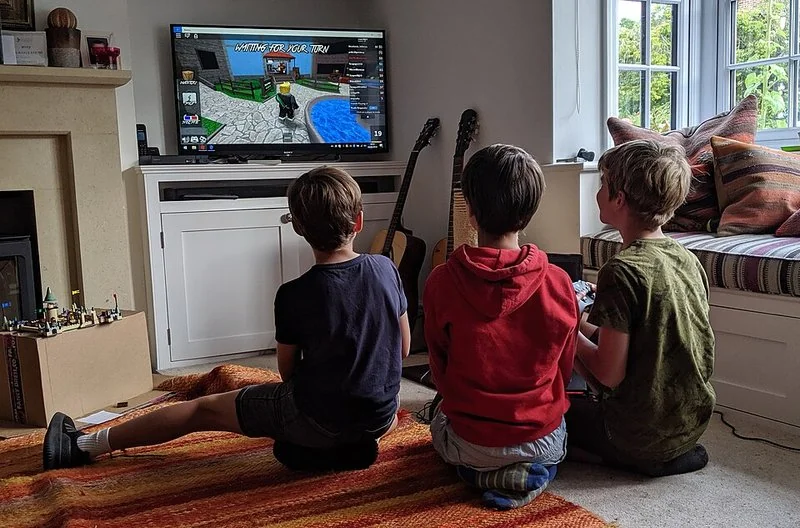 Tres niños juegan a Roblox en una televisión desde el suelo de un salón