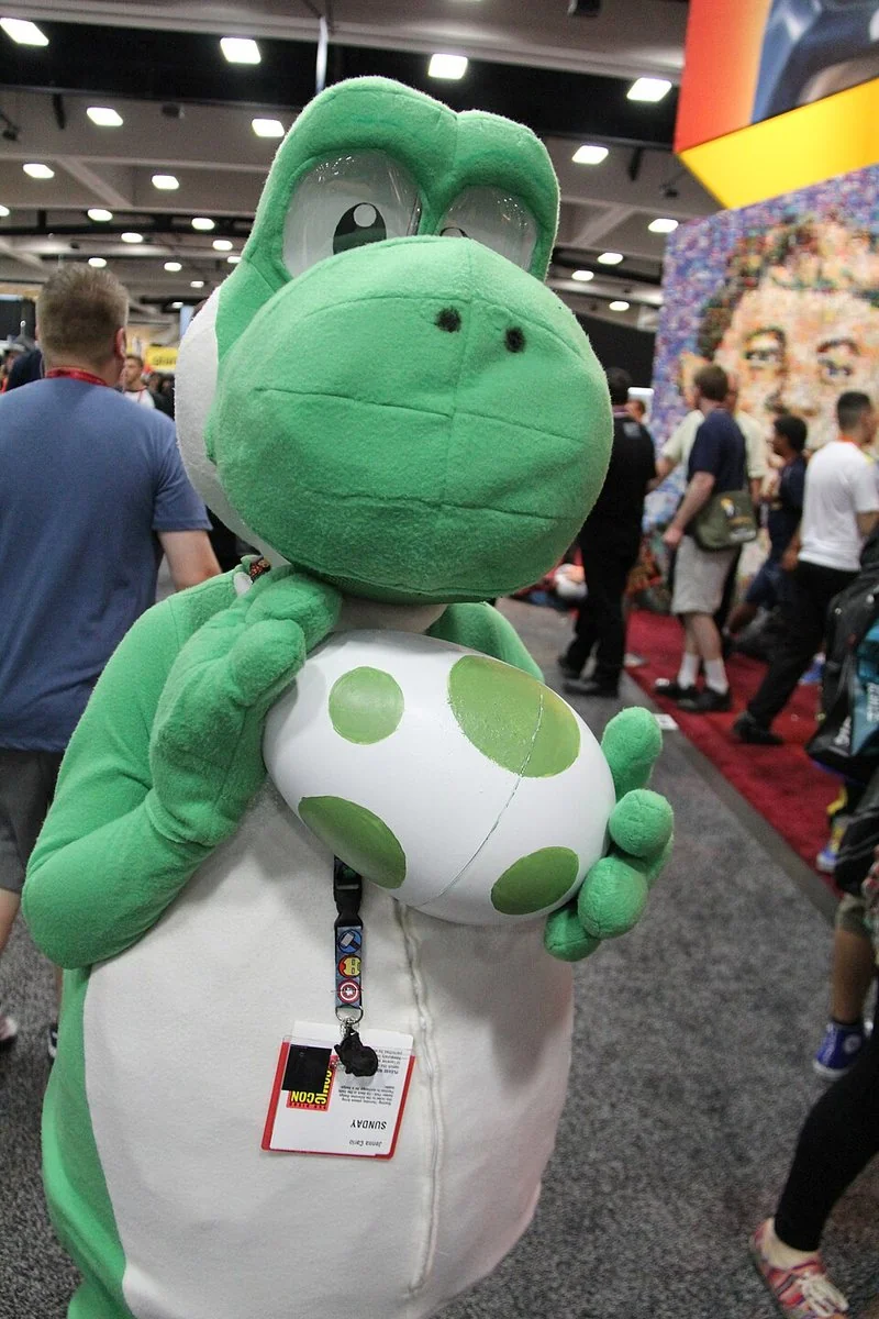 que animal es yoshi, Cosplay de Yoshi verde sosteniendo un huevo de puntos verdes en Comic-Con 2014