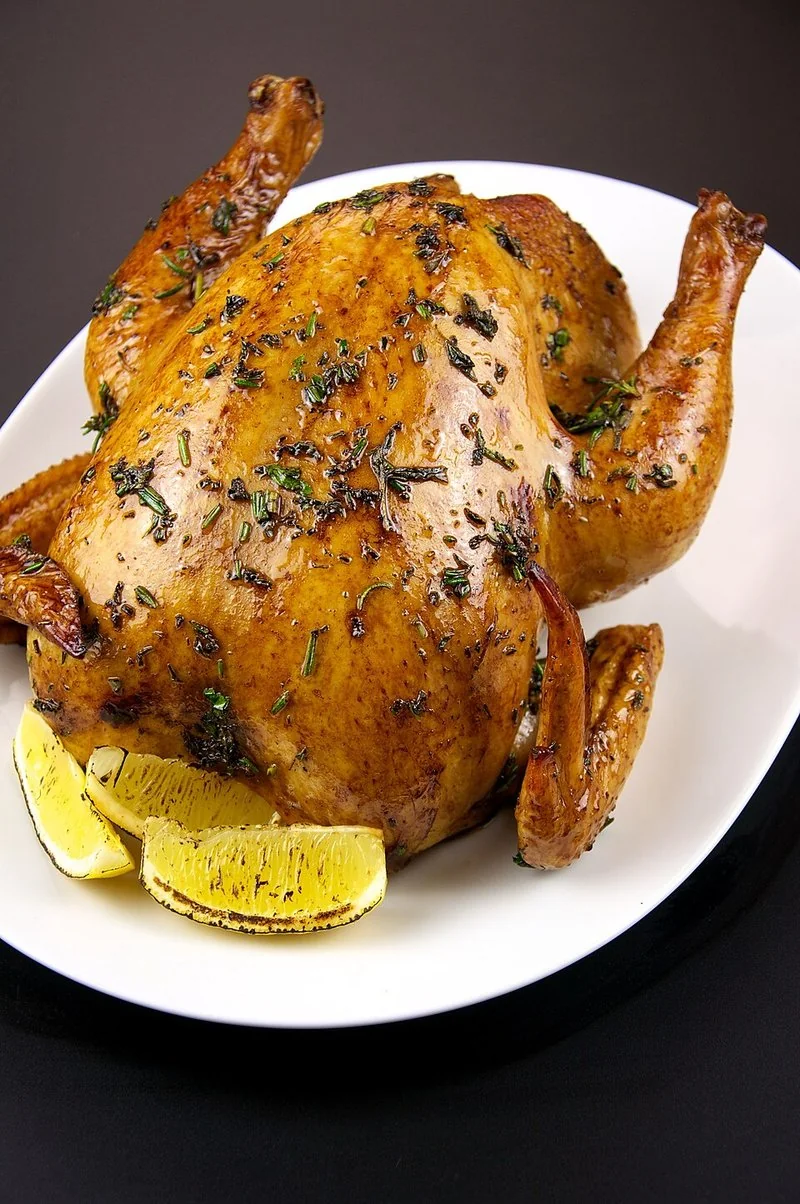 que animal gira 200 veces antes de morir, Pollo asado dorado con hierbas y gajos de limón, servido entero en una fuente blanca