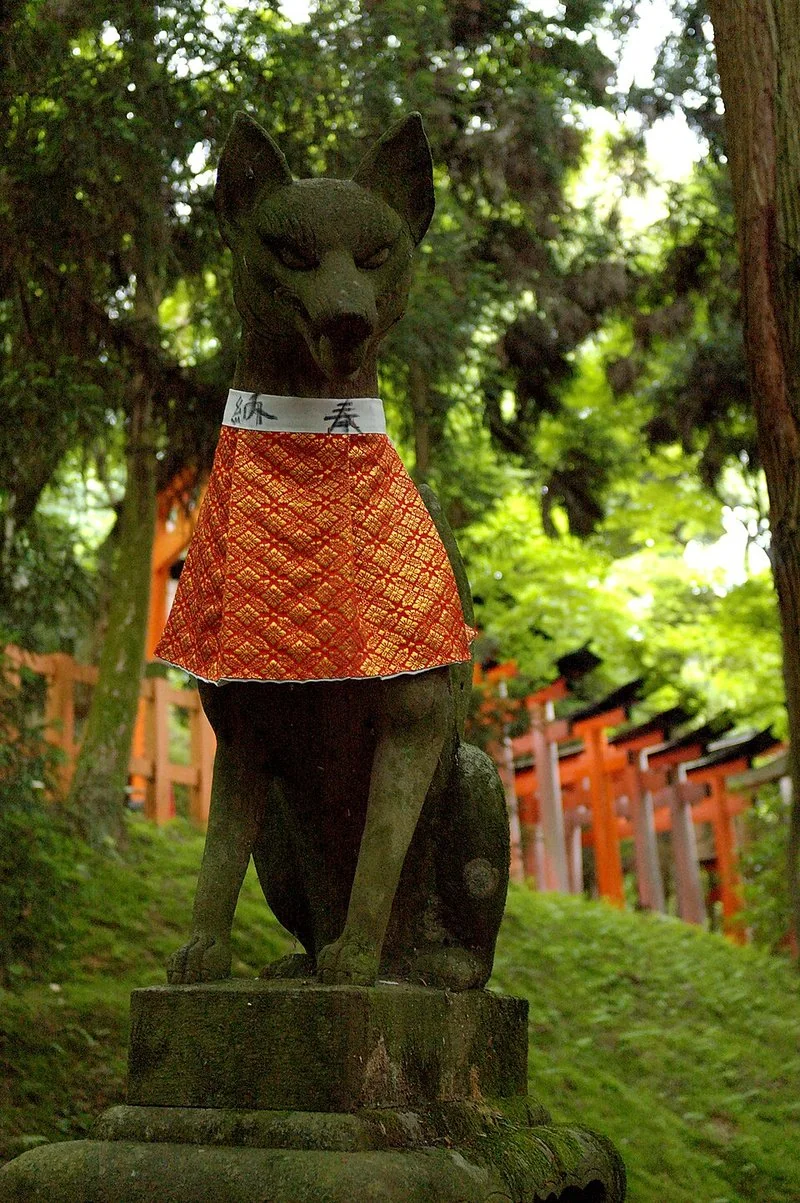 que animal japones soy, Estatua de kitsune con delantal rojo ante los torii del santuario Fushimi Inari