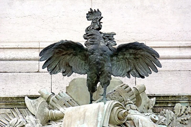 que animal representa a francia, Escultura del gallo galo con alas desplegadas sobre trofeos militares en un monumento francés