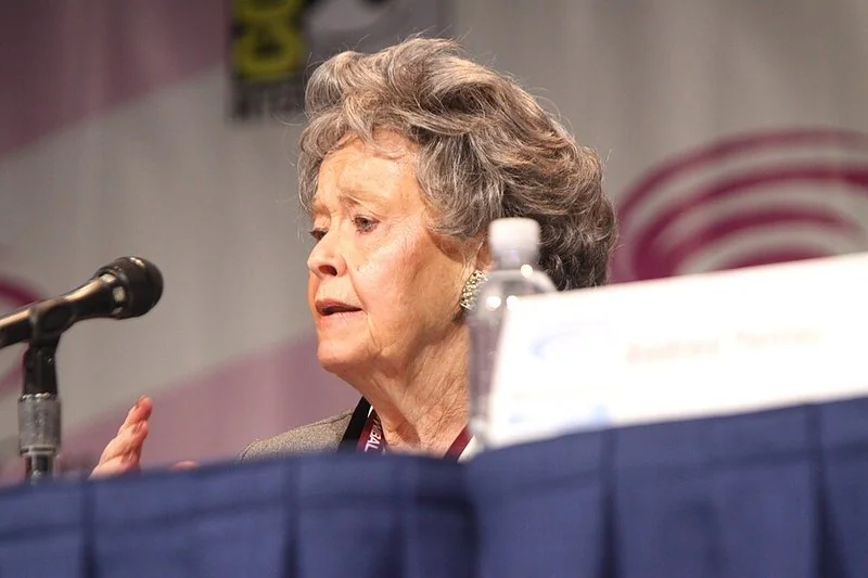 que hicieron los warren, Lorraine Warren interviniendo ante el público en un panel con micrófono y botella de agua sobre la mesa