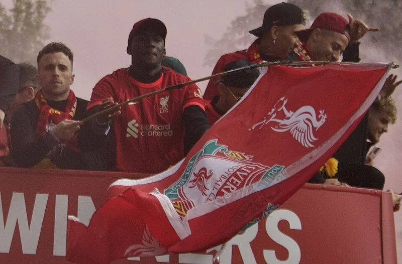 Diogo Jota, con la equipación roja del Liverpool, sujeta la bandera del club durante la parade celebrista de los 'Reds' sobre el autobús, junto a sus compañeros