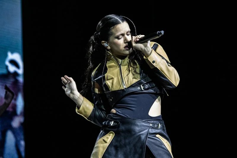 Rosalía en concierto en Chile (2022), cantando con micrófono y vestida con un conjunto de cuero negro y dorado