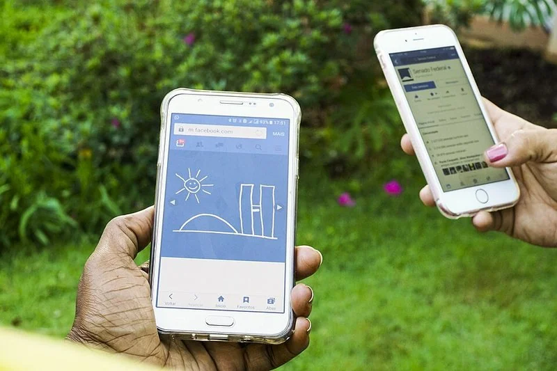 Dos manos usando teléfonos iPhone con iOS para navegar por la web al aire libre